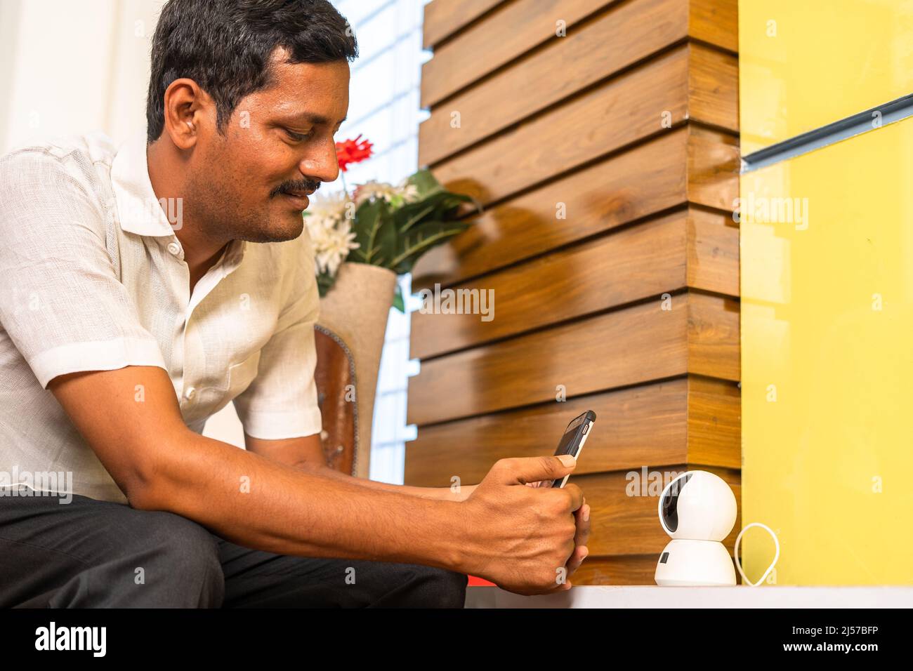 le propriétaire d'une maison connecte une caméra de vidéosurveillance intelligente sur un téléphone portable à la maison - concept de sécurité, de sécurité et de technologie de maison intelligente. Banque D'Images