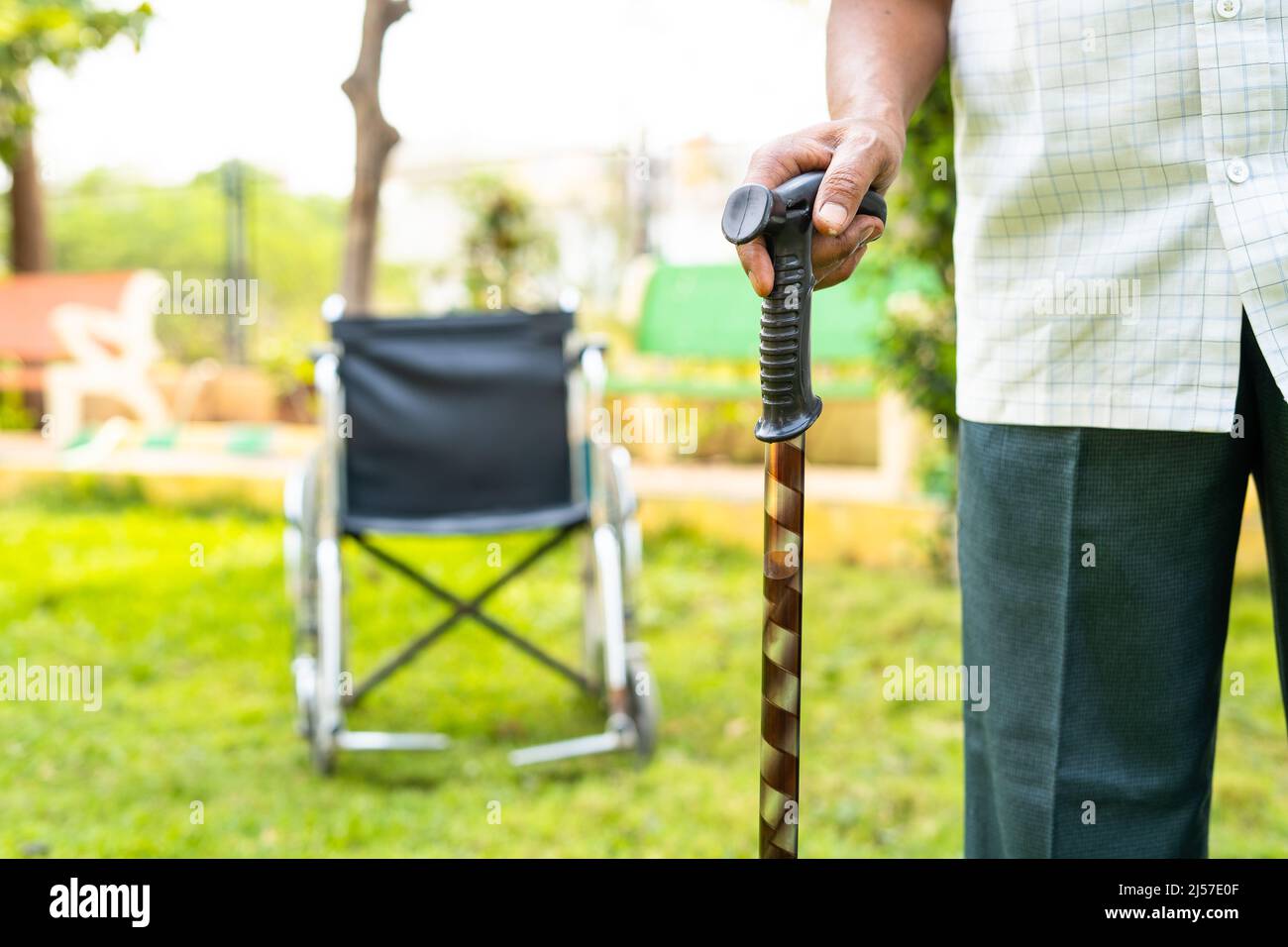 Le vieil homme waliking en utilisant le bâton devant le fauteuil roulant dans le jardin de l'hôpital - concept de soins de santé, de récupération, de traitement. Banque D'Images