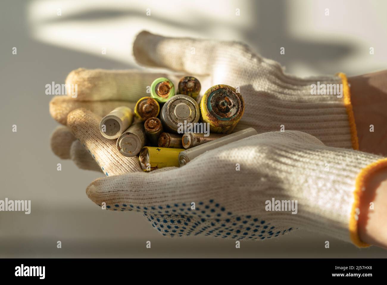Gros plan des mains des femmes dans des gants de protection en coton tenant le tas de piles alcalines usagées Banque D'Images