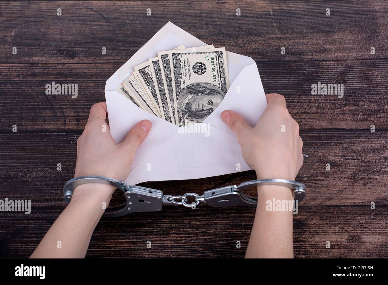 Les mains menottées tiennent une enveloppe blanche ouverte avec des dollars sur un fond en bois sombre Banque D'Images