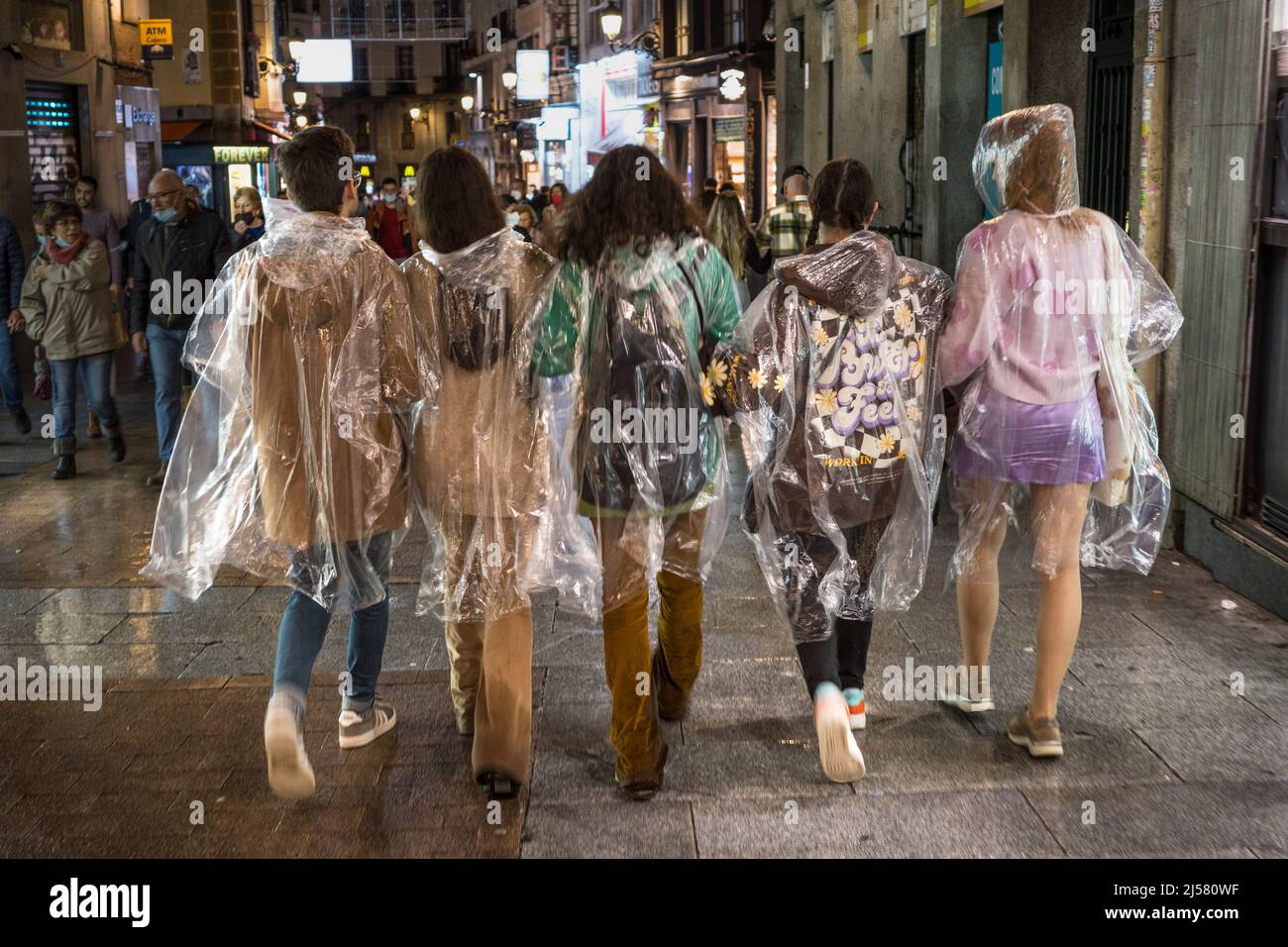 Un groupe de jeunes marchant sous la pluie portant des manteaux de pluie jetables en plastique transparent, Madrid, Espagne. Banque D'Images