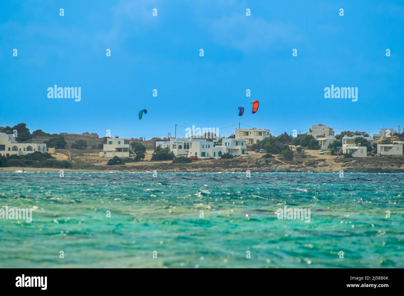 Kitesurfers en long coup devant des maisons blanches, style grec typique de bâtiment. Vue depuis une position basse juste au-dessus du niveau de la mer, Grèce Banque D'Images