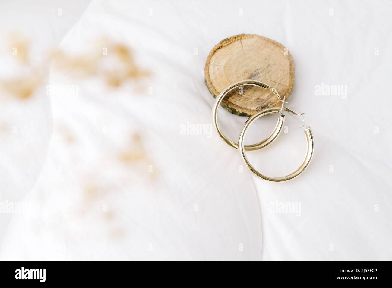 Bijoux fantaisie, boucles d'oreilles de bijouterie dorées sur fond blanc.Podium en bois et fleurs sèches. Banque D'Images