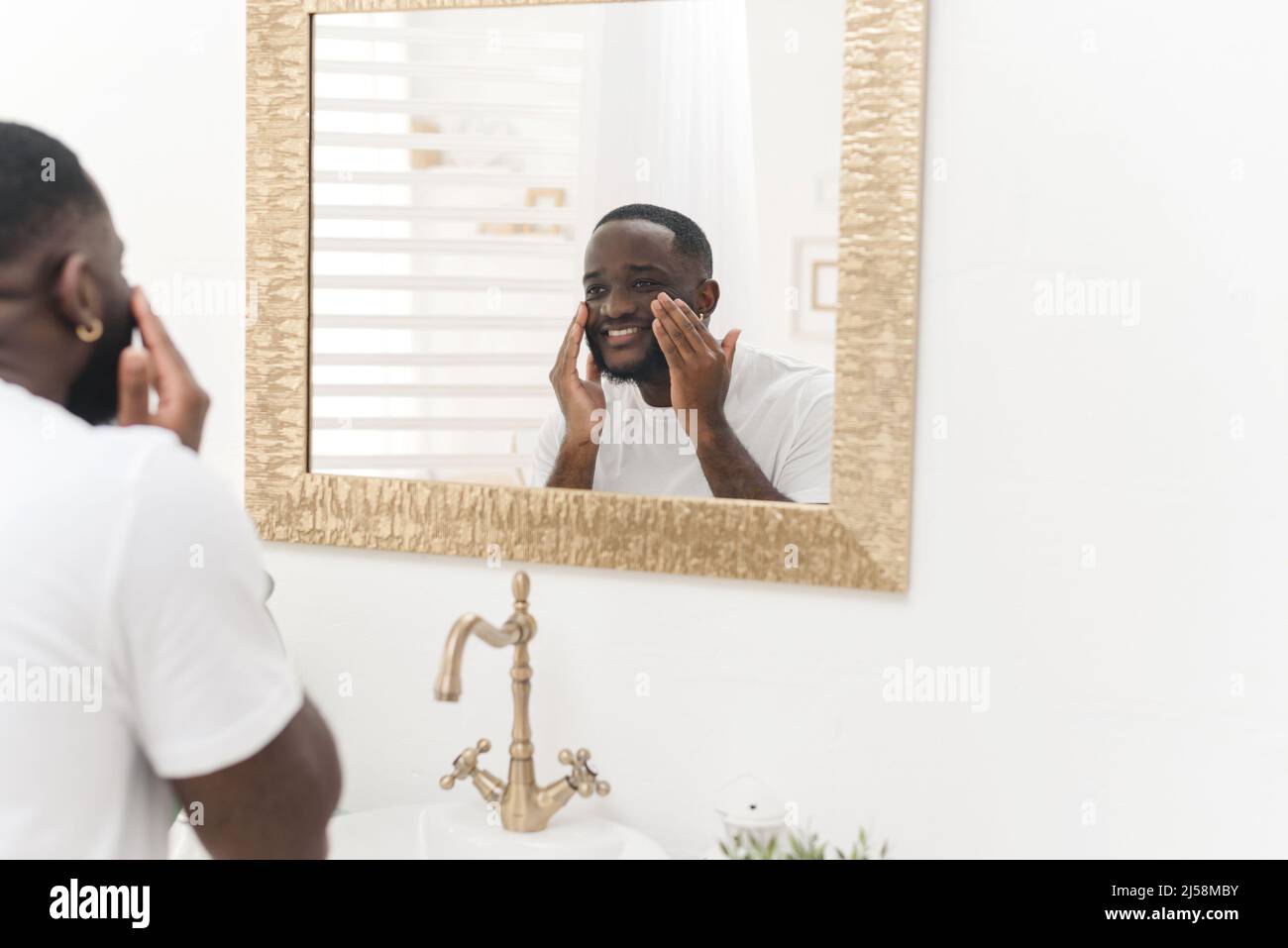 Noir heureux homme lave son visage dans la salle de bains. Routine quotidienne. Banque D'Images