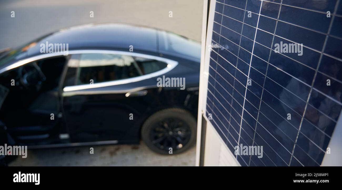 Sur le fond flou d'une voiture d'élite noire, vue rapprochée d'un panneau solaire. Concept écologique véhicule électrique comme alternative au transport à carburant. Banque D'Images