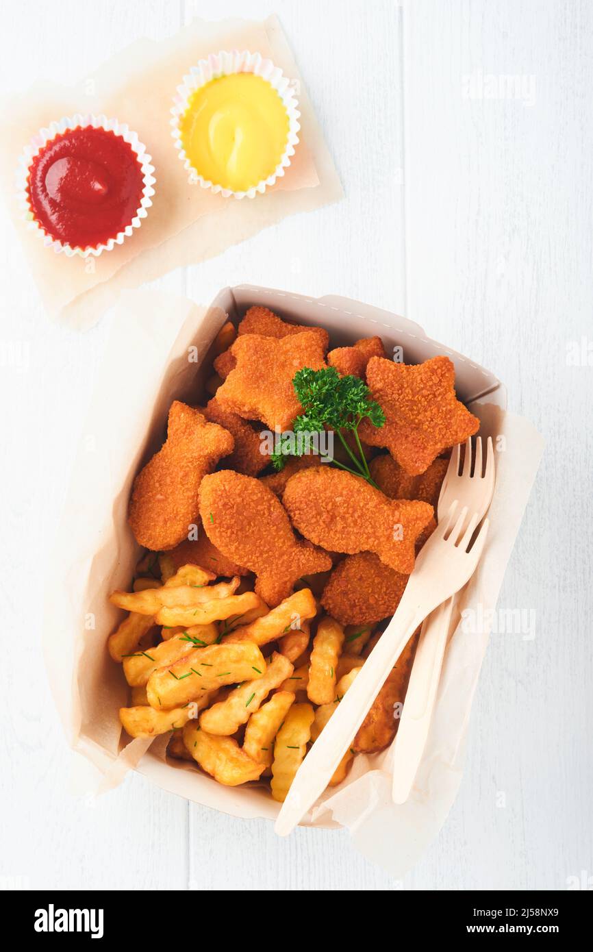 Fish and Chips, restauration rapide britannique. Bâtonnets de poisson avec frites sur une assiette en papier à emporter sur fond en bois blanc. Authentique britannique traditionnel Banque D'Images