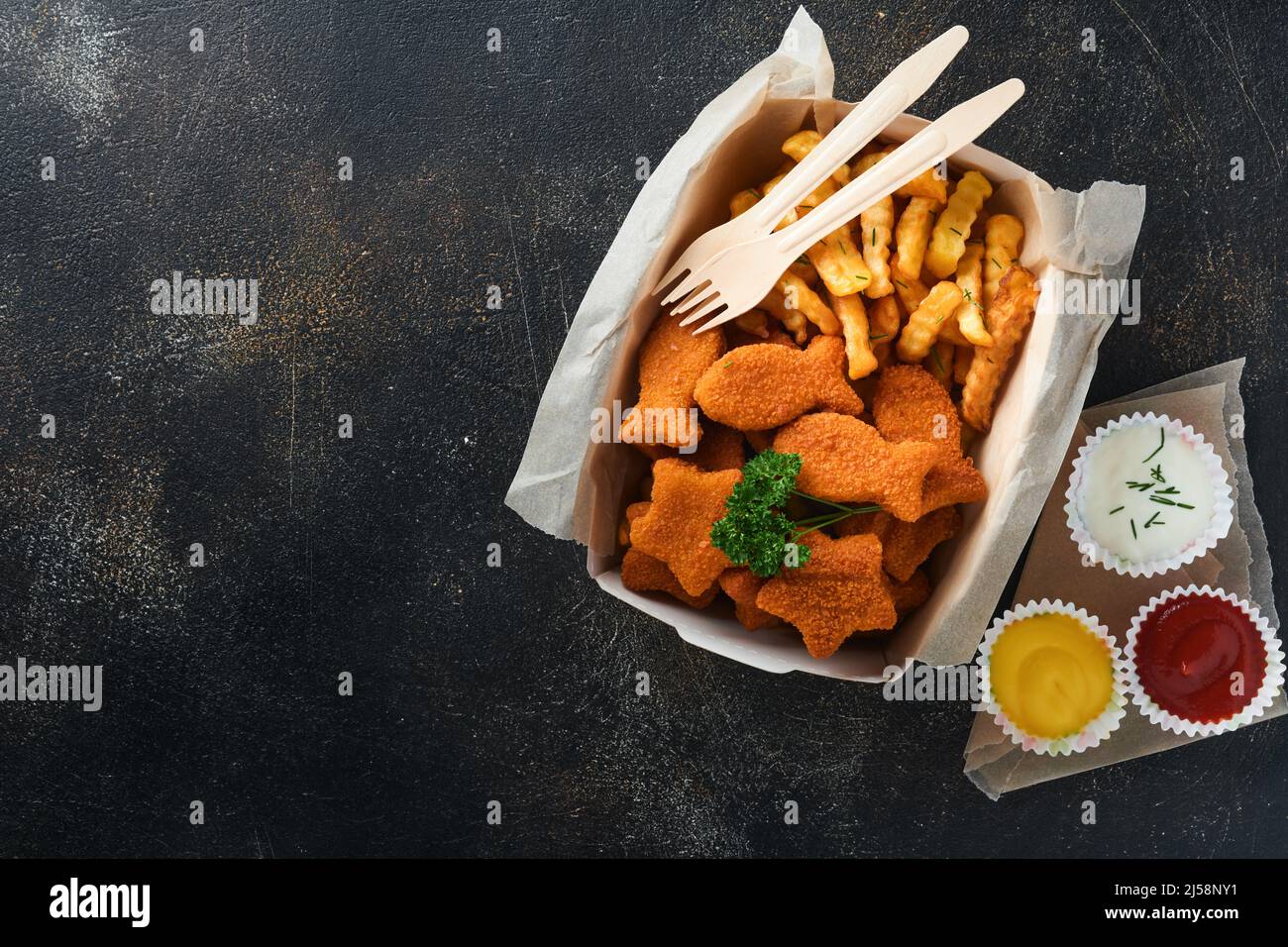 Fish and Chips, restauration rapide britannique. Bâtonnets de poisson avec frites sur une plaque de papier à emporter sur fond de béton ancien sombre. Traditionnel anglais authe Banque D'Images