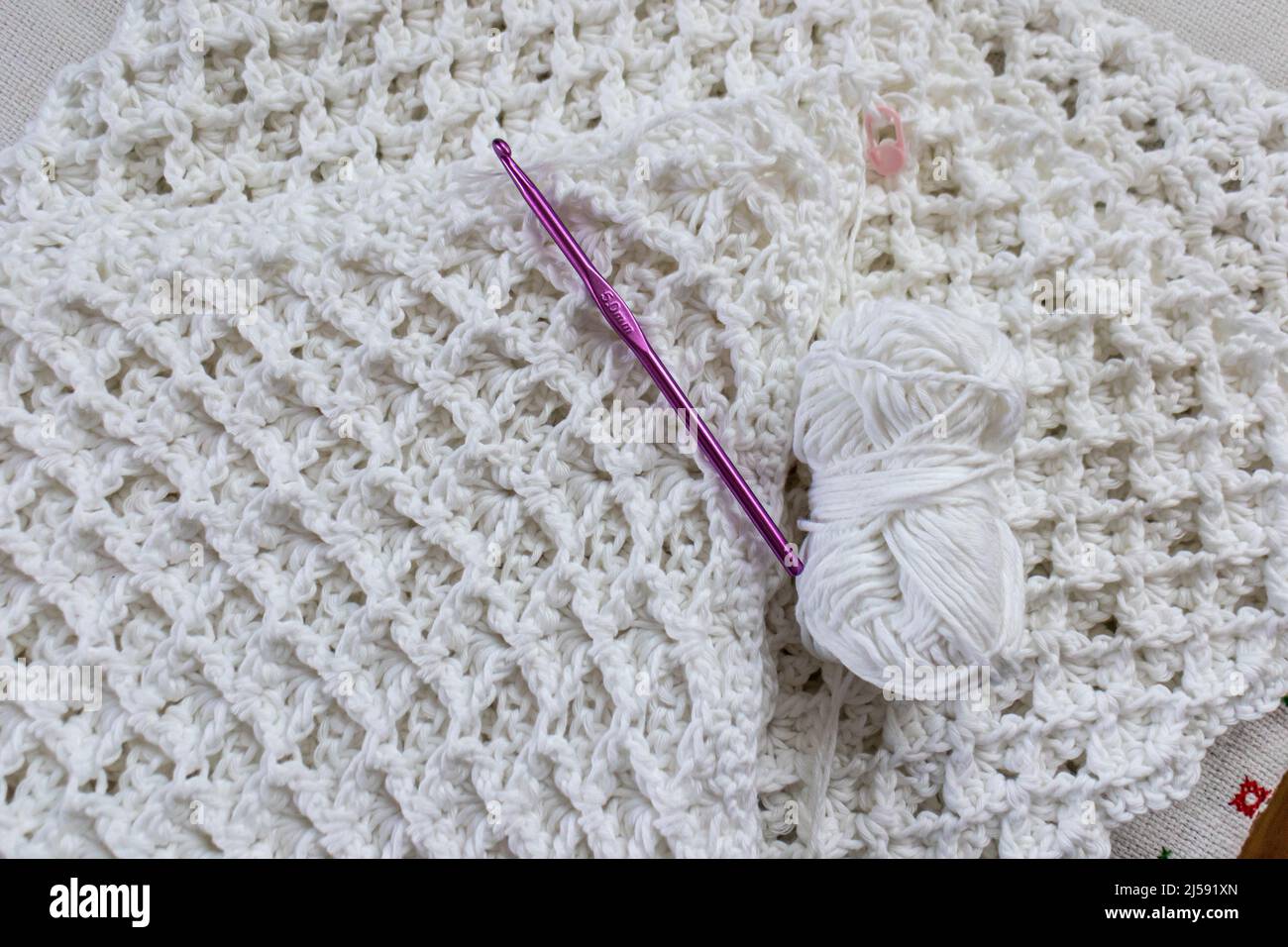 Vue de dessus d'une boule de fil, crochet en crochet violet de 5 mm, ruban  de mesure jaune, marqueur rose sur une couverture en coton blanc  partiellement fini, original en relief Photo