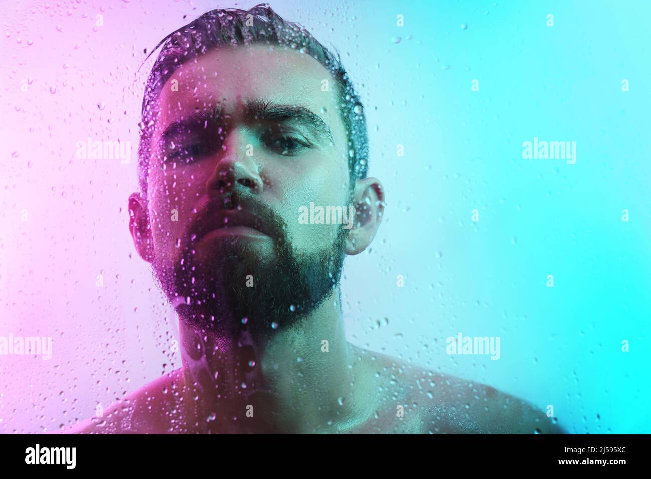 Portrait du jeune homme beau à travers le verre humide dans la lumière néon Banque D'Images