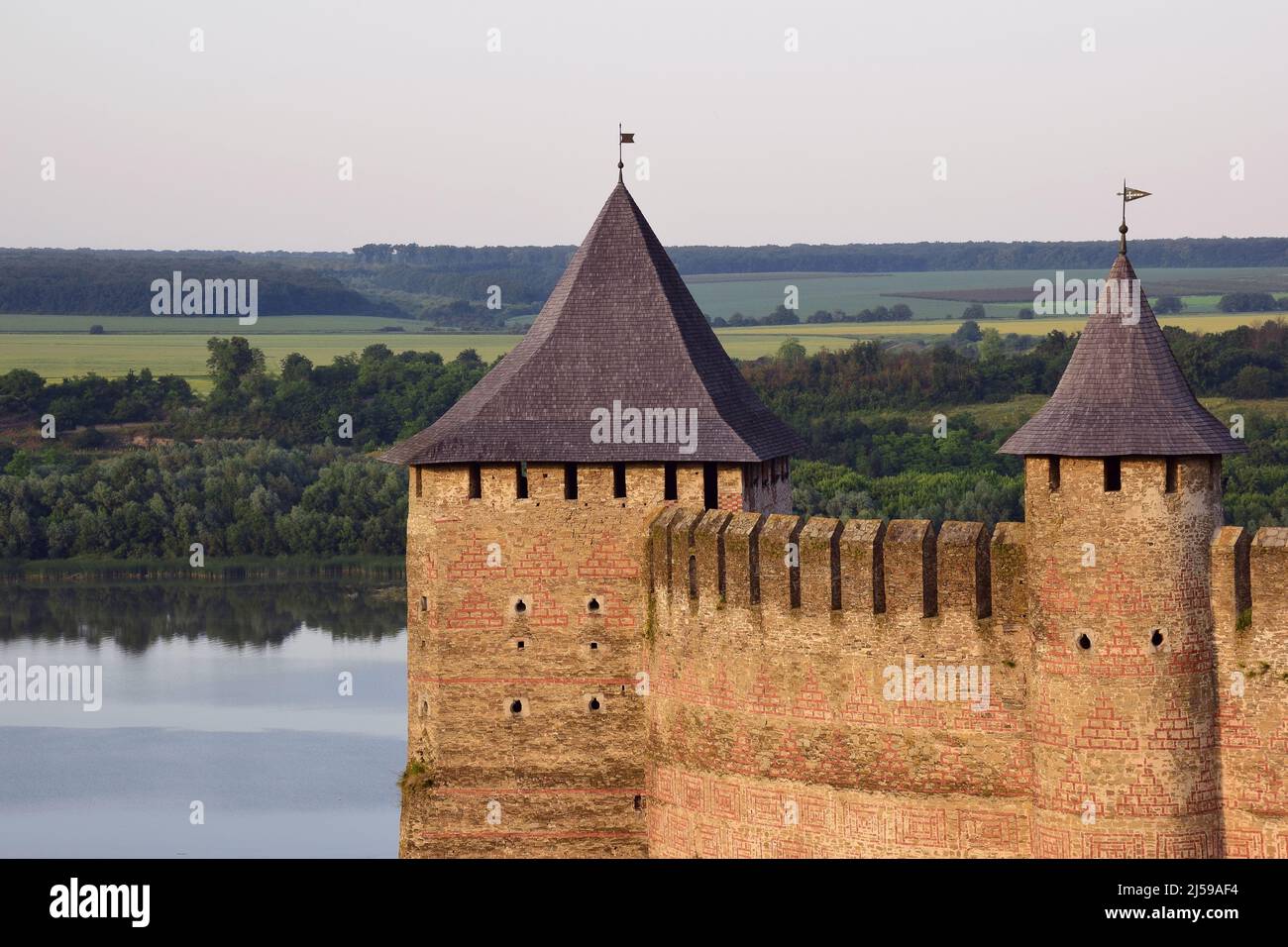 La partie supérieure du mur en pierre d'une forteresse médiévale avec des remparts, des échappatoires et des tours. Derrière elle se trouve une rivière et une forêt Banque D'Images