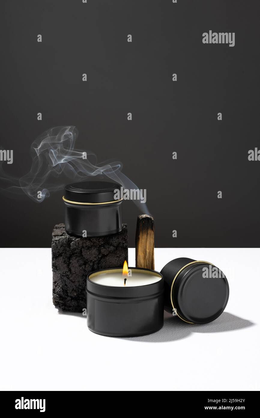 Composition de Palo santo en feu et de bougies en cire de soja dans des pots noirs en métal élégants sur une table blanche sur fond sombre. ECO Banque D'Images