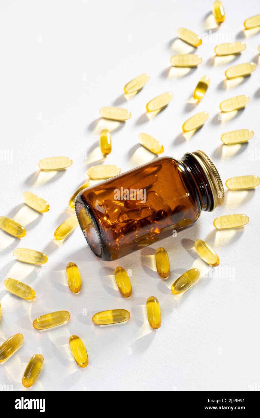 La lumière du soleil traverse une bouteille avec des pilules et des capsules Omega-3 sur fond blanc. Caustiques lumière. Gels à base d'huile de poisson. Support médical Banque D'Images