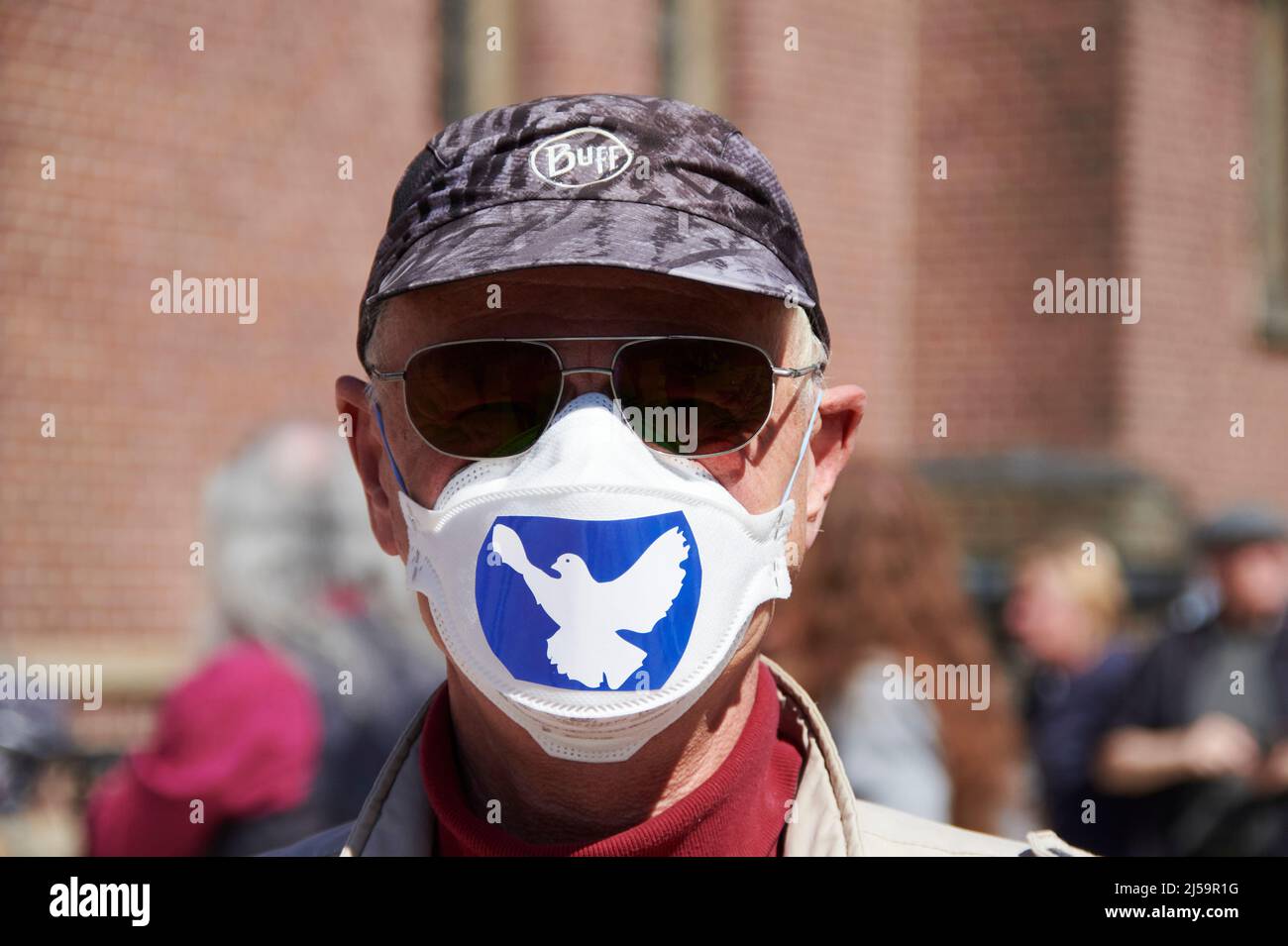 Ein Mann der an einem Ostermarsch teilnimmt traegt Sonnebrille, Capie, und eine FFP 2 Maske mit einem Aufkleber auf dem die Friedenstaube zu sehen ist Banque D'Images