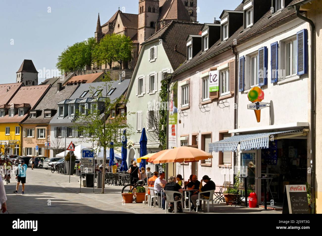 Breisach, Allemagne - avril 2022: Personnes assis à l'extérieur d'un café sur la route principale à travers la ville. En arrière-plan se trouve la cathédrale Saint-Étienne Banque D'Images