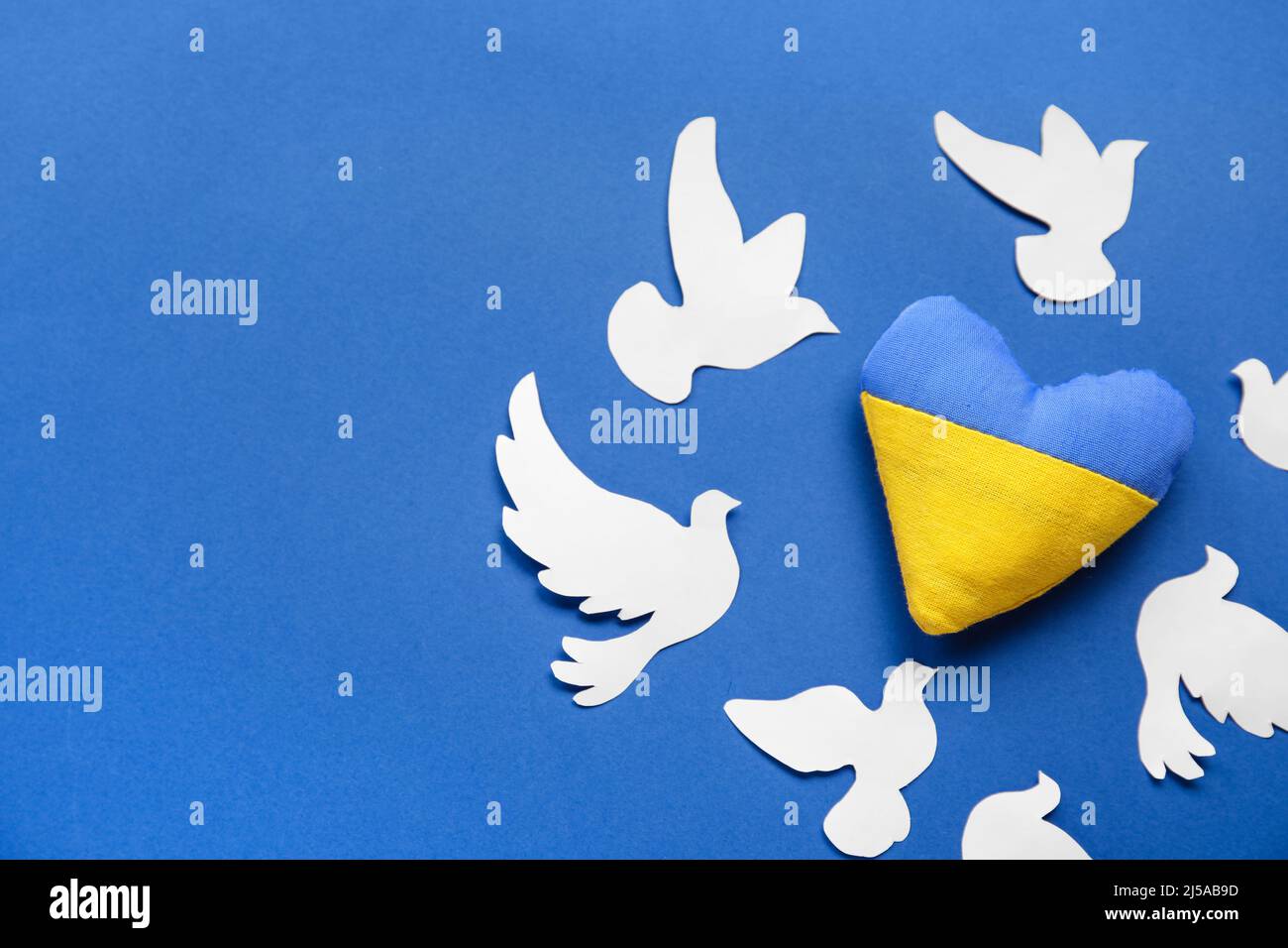 Coeur aux couleurs du drapeau ukrainien et colombes en papier comme symbole de paix sur fond bleu Banque D'Images