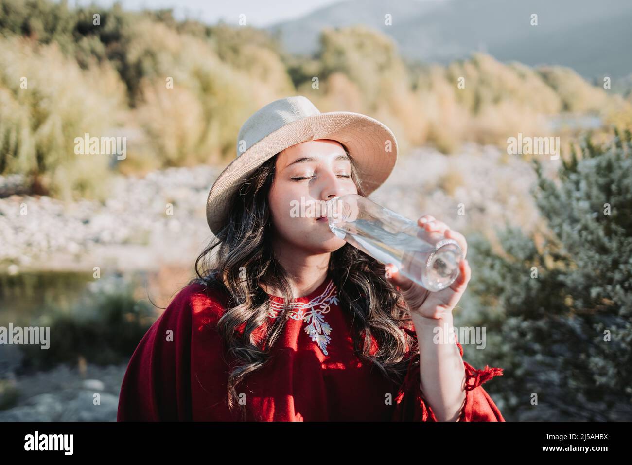 Jeune femme latino-américaine utilisant des vêtements traditionnels, buvant de l'eau dans une bouteille de verre. Banque D'Images