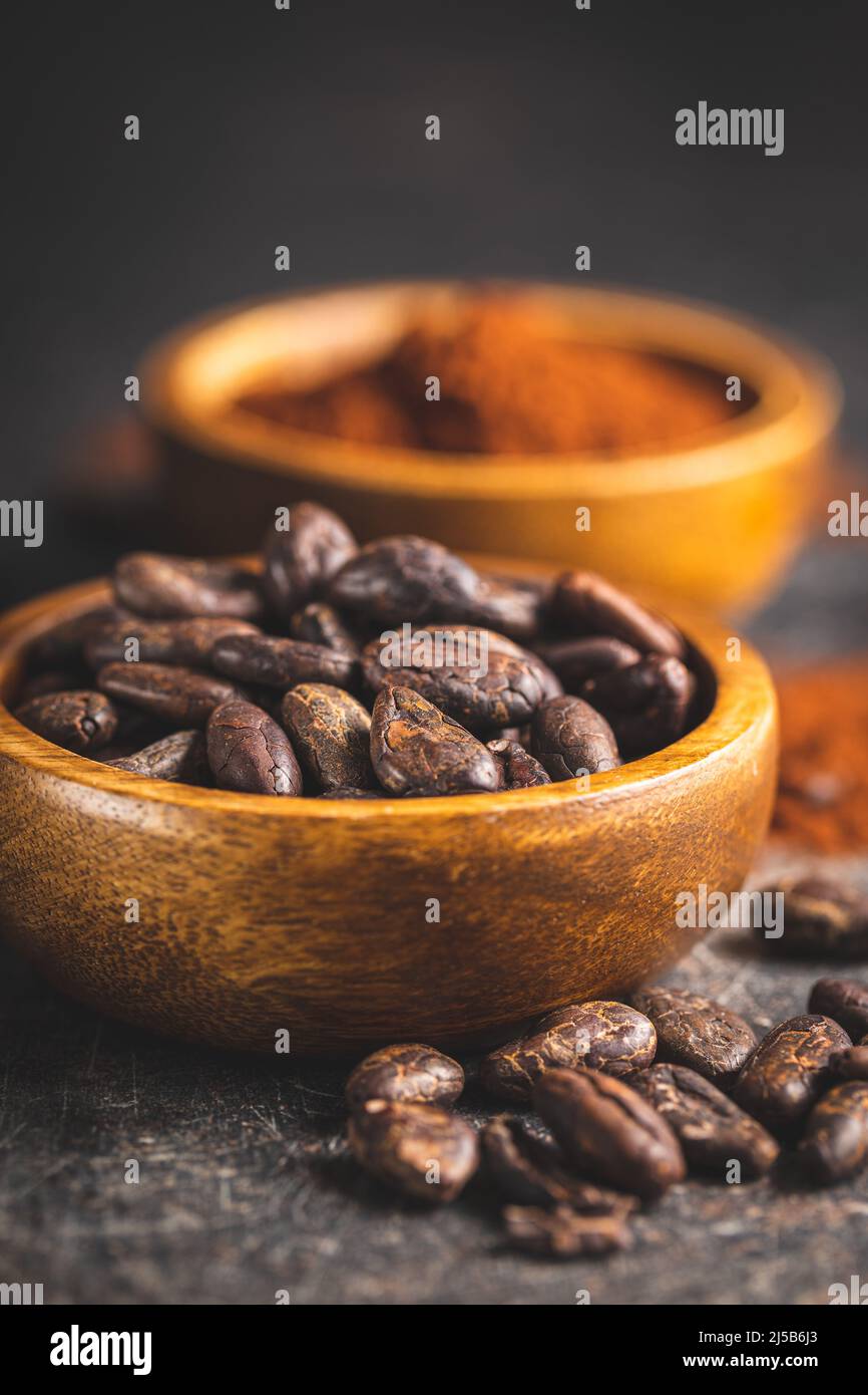 Fèves de cacao et poudre de cacao dans des bols en bois sur une table noire. Banque D'Images
