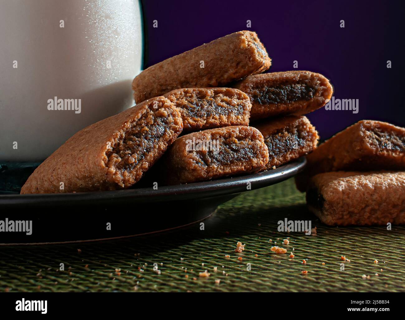 Barres à biscuit de la Fig une assiette noire avec un verre de glace ou de lait froid, sur un linge de table vert avec un rouge violet foncé Banque D'Images