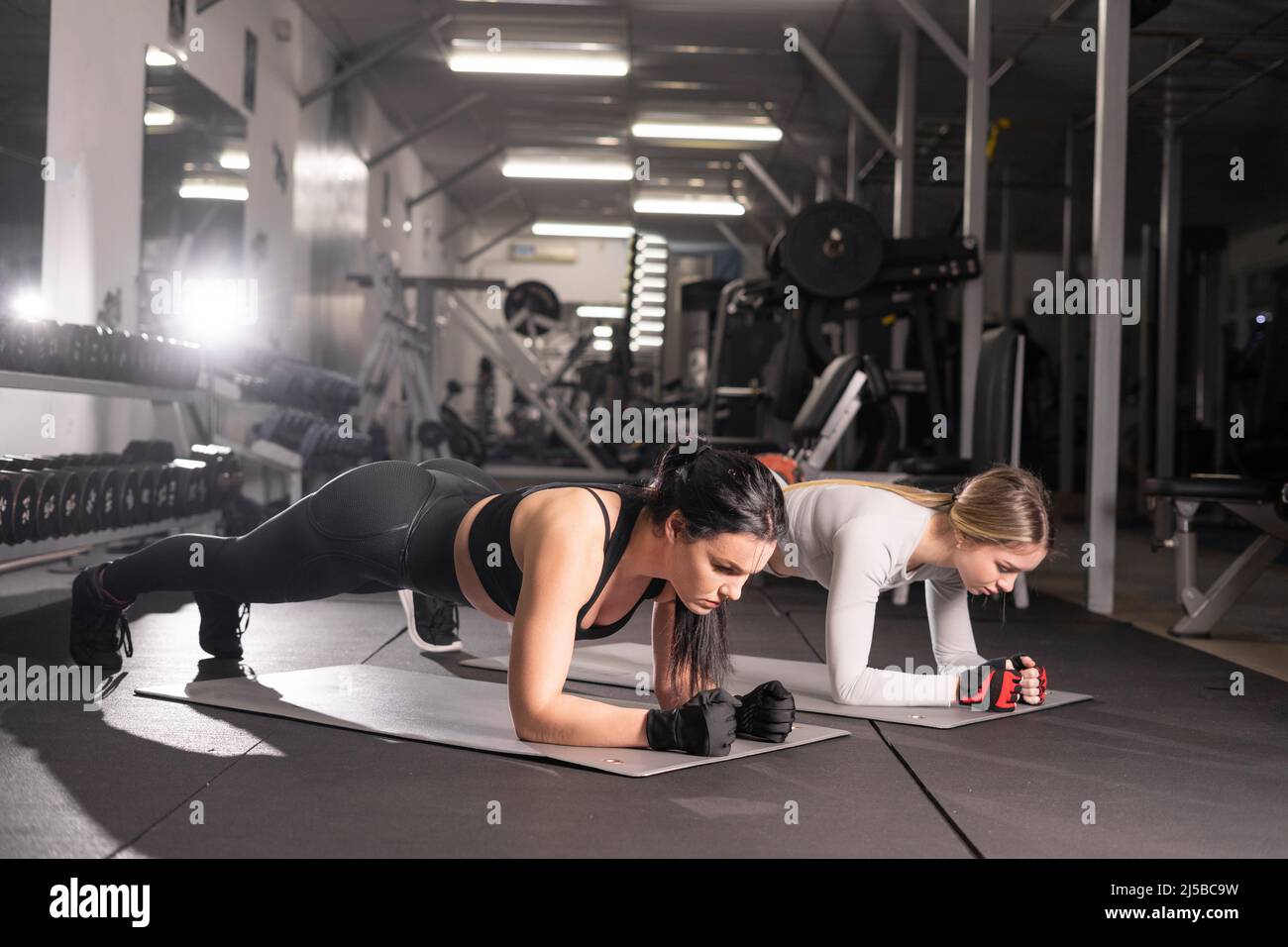 deux jeunes femmes attirantes sont engagées dans l'entraînement dans la salle de gym planche d'exercice pour les muscles abdominaux. Style de vie sain, concept de gymnastique, espace de copie Banque D'Images
