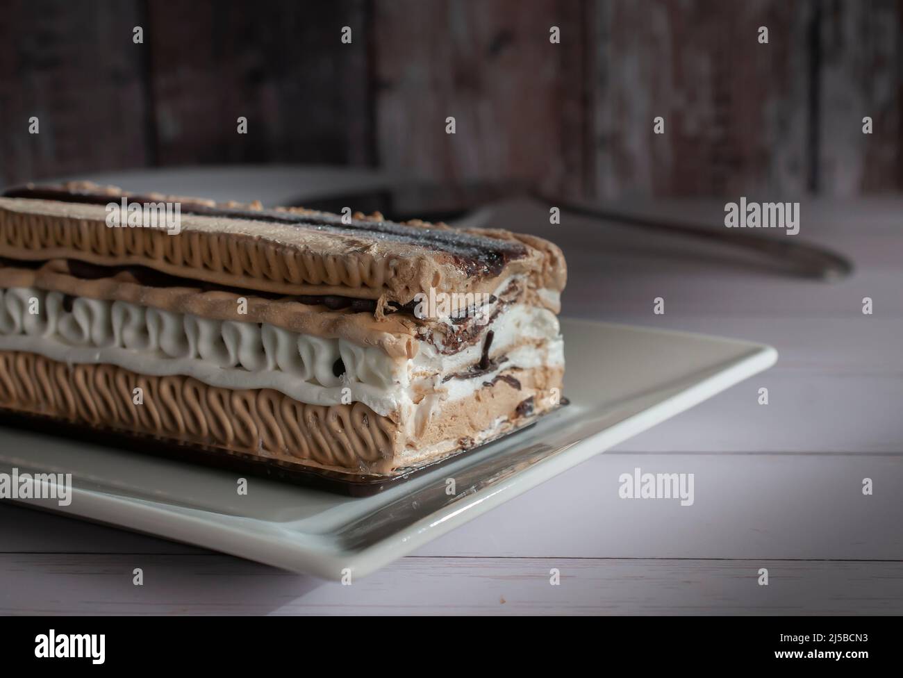 Un gâteau à la crème glacée au café Moka de forme rectangulaire sur une assiette blanche avec un mur en bois vintage en arrière-plan Banque D'Images