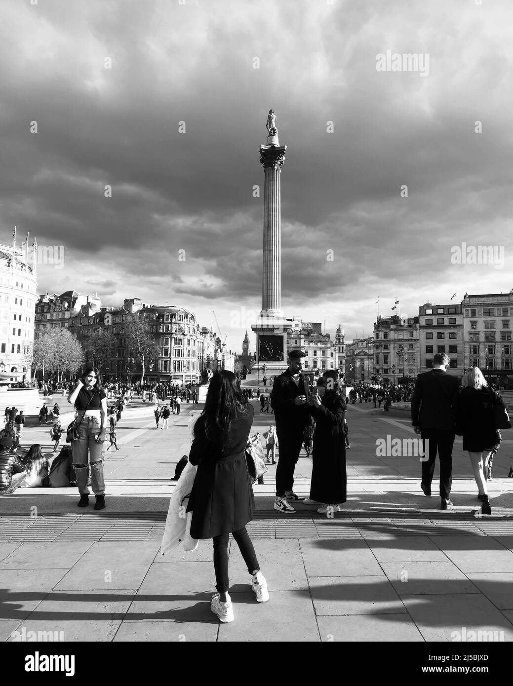 Touristes ayant des photos prises à Trafalgar Square avec Nelsons colonne derrière et ciel spectaculaire au-dessus. Monochrome. Londres. Banque D'Images