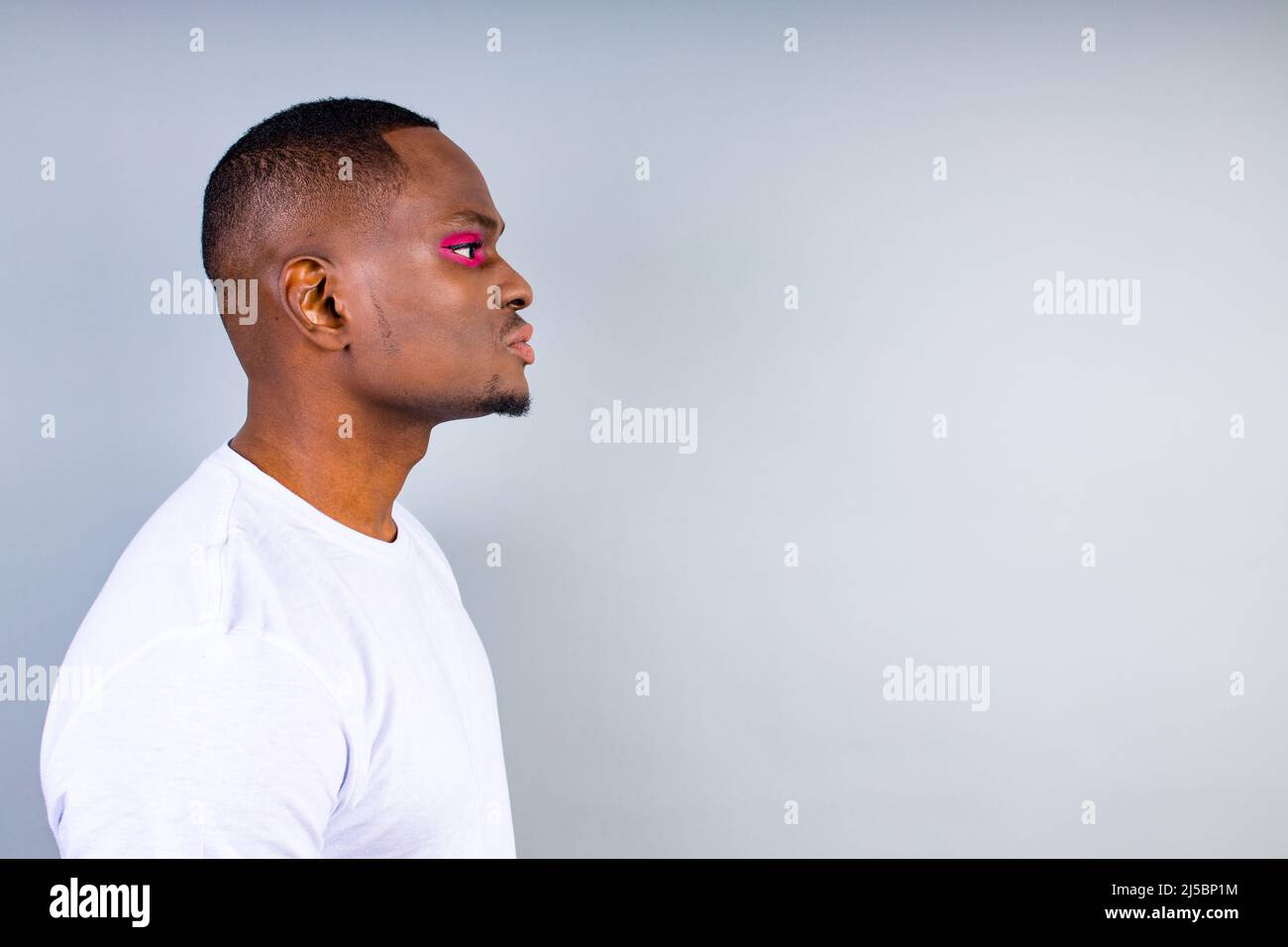 afro american man en t-shirt blanc style décontracté avec fard à paupières rose et rouge à lèvres crossdressing en arrière-plan de studio de mode Banque D'Images