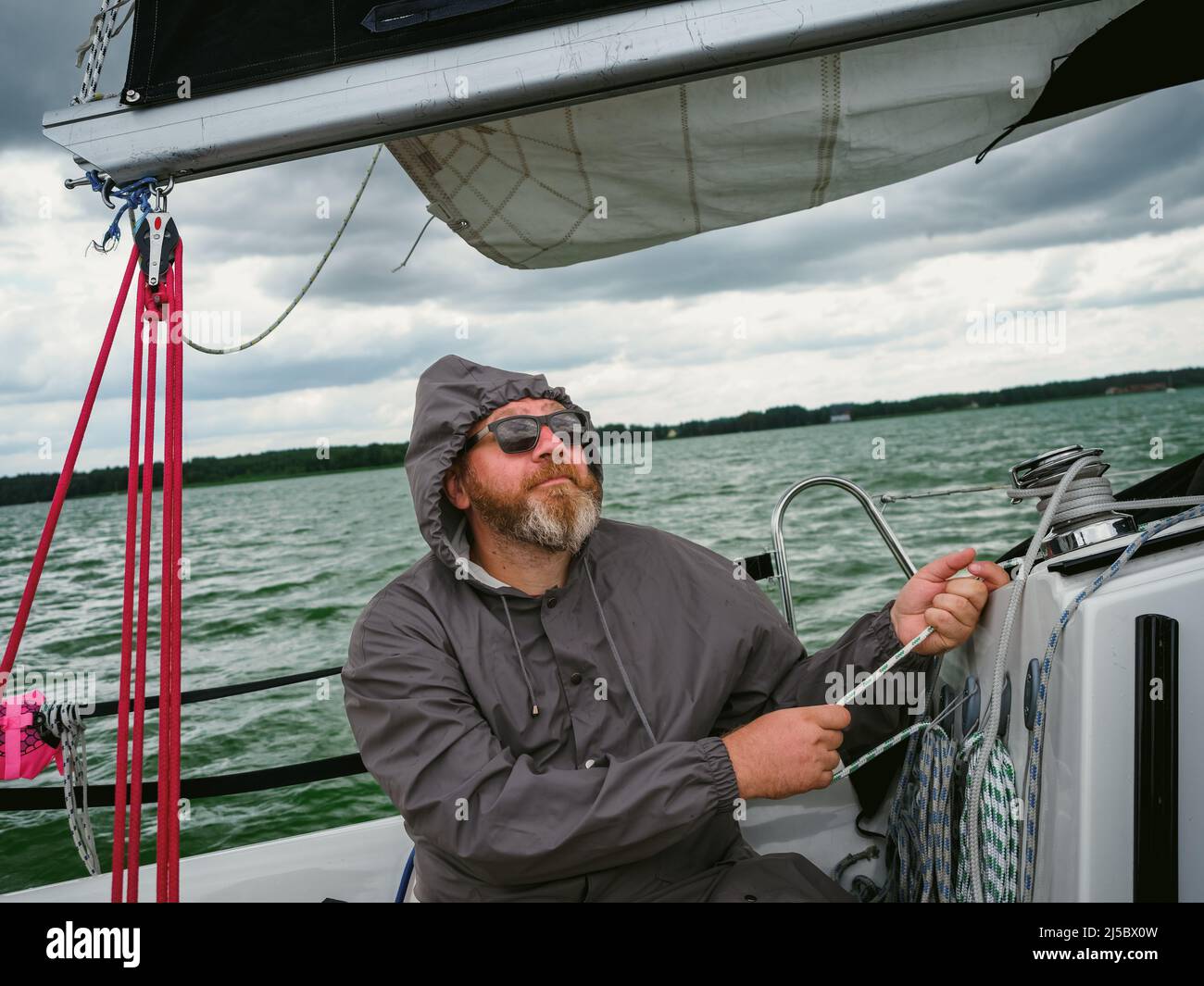 voile sur un yacht par temps pluvieux. homme adulte utilisant un treuil pour tirer une corde sur un voilier ou un yacht à voile pour contrôler une voile de yacht, le yacht navigue dans Banque D'Images