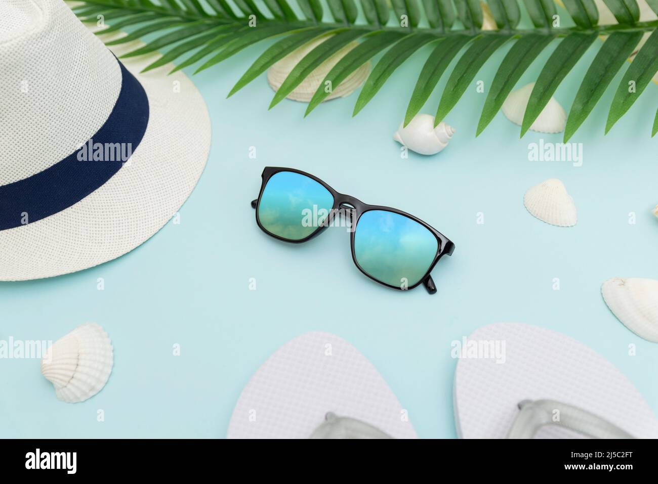 Accessoires de plage d'été sur fond bleu. Chapeau, lunettes, pantoufles, coquilles et feuilles de palmier Banque D'Images