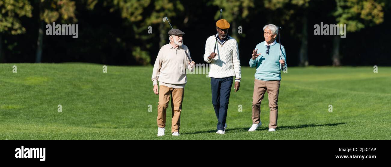 amis séniors interraciaux marchant avec des clubs de golf sur le terrain, bannière Banque D'Images