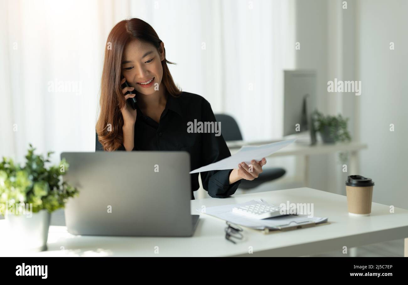 Jeune femme d'affaires asiatique utilisant l'ordinateur dans le bureau avec ordinateur portable et les appels sur le téléphone mobile, concept de comptabilité financière. Banque D'Images