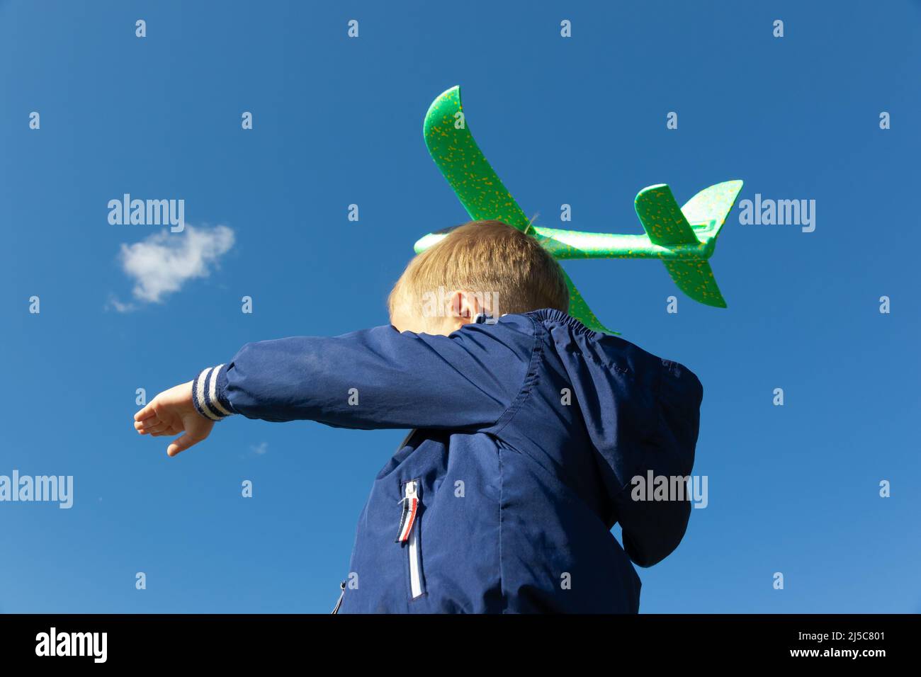 Un garçon d'âge préscolaire de six ans, dans une veste bleue, lance un avion jouet dans la nature sur fond de ciel bleu clair lors d'une journée d'été. La lumière Banque D'Images