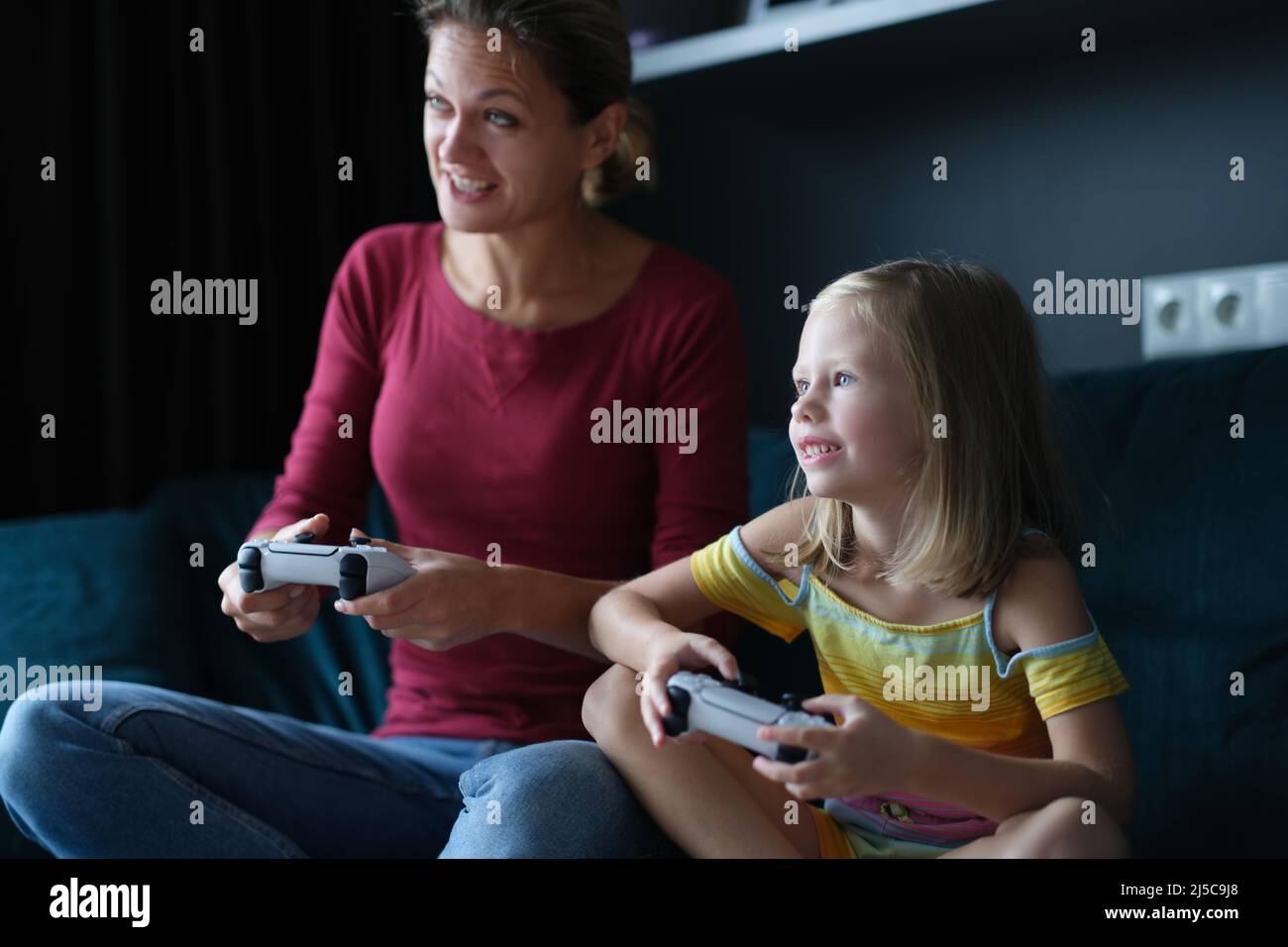 Maman et fille tiennent des manettes de jeu et jouent à des jeux en ligne Banque D'Images