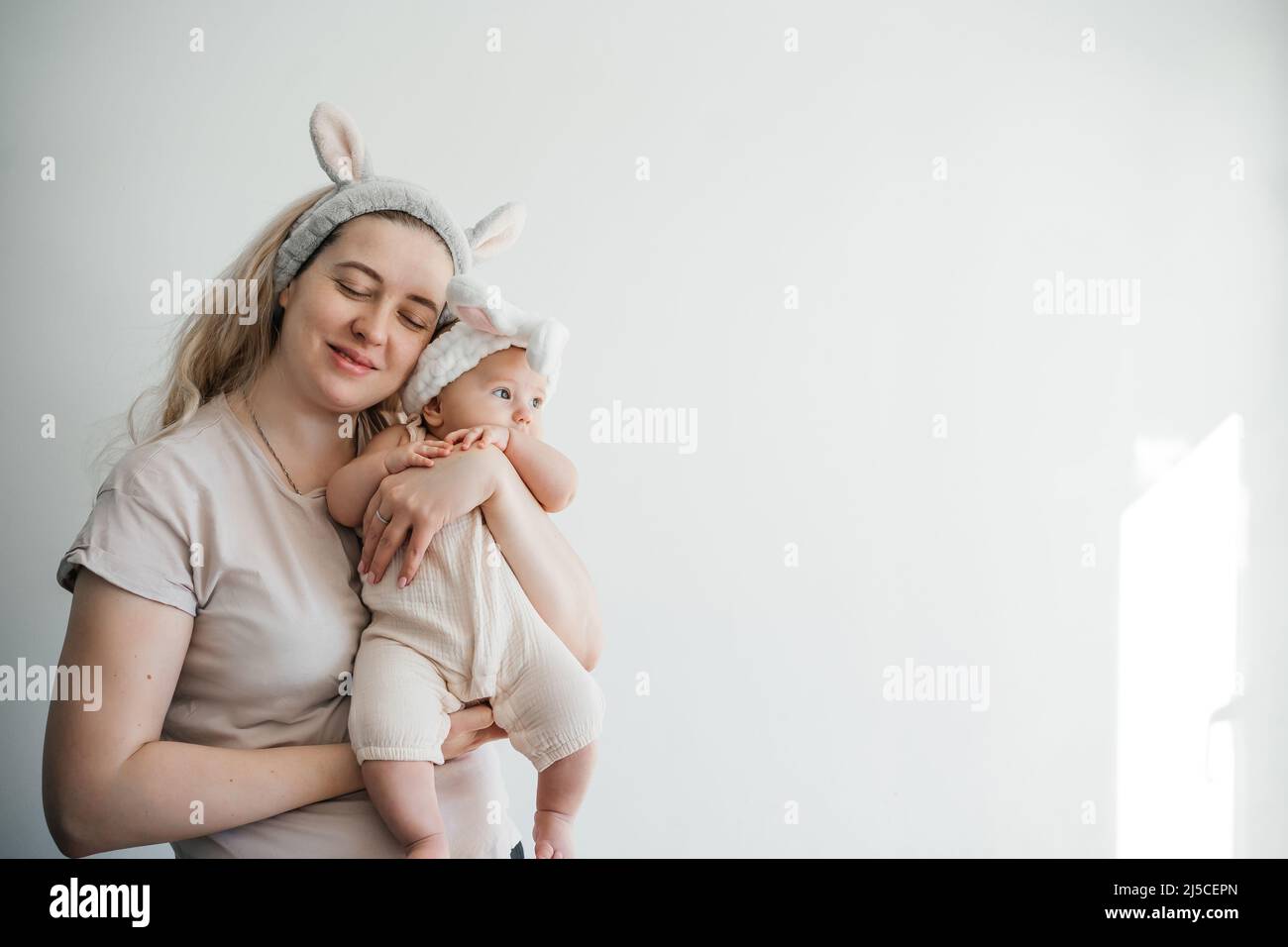 Maman blonde et fille de nouveau-né en blanc avec des oreilles de lapin photo sur un fond clair célébrer Pâques Banque D'Images
