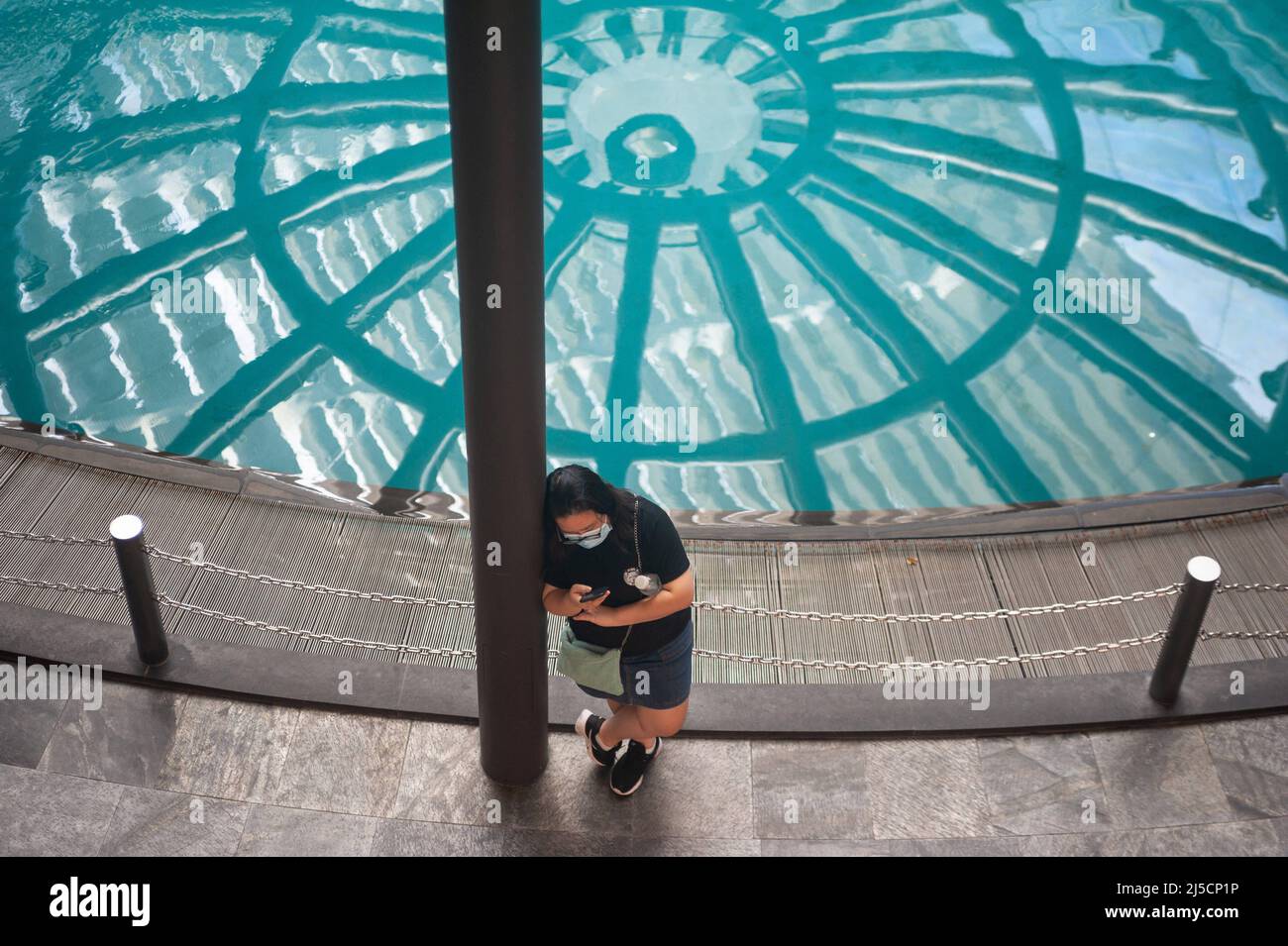 25 juin 2020, Singapour, République de Singapour, Asie - Une femme portant un protège-bouche se tient près d'une piscine d'eau au centre commercial Marina Bay Sands (The Shoppes) Regarder son téléphone portable peu après que les restrictions de couvre-feu ont été levées dans le contexte d'une pandémie de Corona (Covid-19) qui a vu la plupart des magasins fermés pendant plus de deux mois et la vie publique sévèrement réduite. [traduction automatique] Banque D'Images