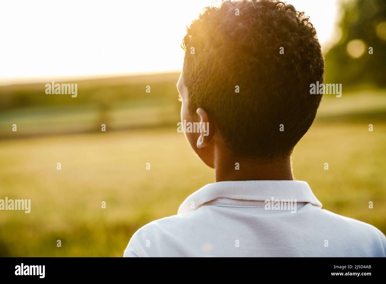 Garçon noir portant une chemise blanche regardant le coucher du soleil sur le terrain d'été Banque D'Images