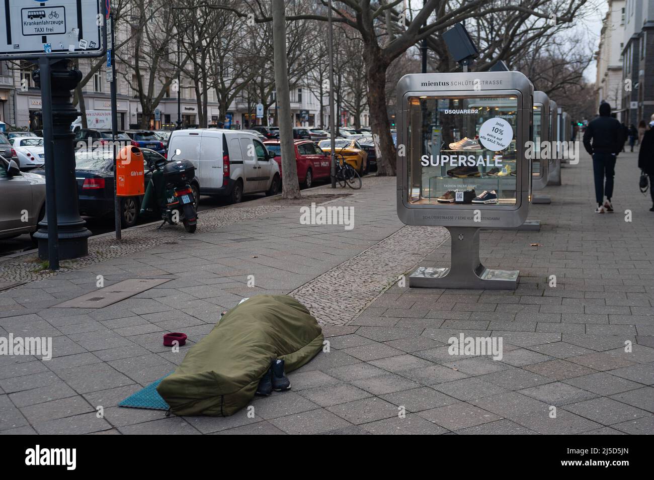 02/05/2022, Berlin, Allemagne, Europe - Un homme sans domicile dort dans son sac de couchage sur le trottoir devant un magasin de mode sur Kurfuerstendamm. [traduction automatique] Banque D'Images