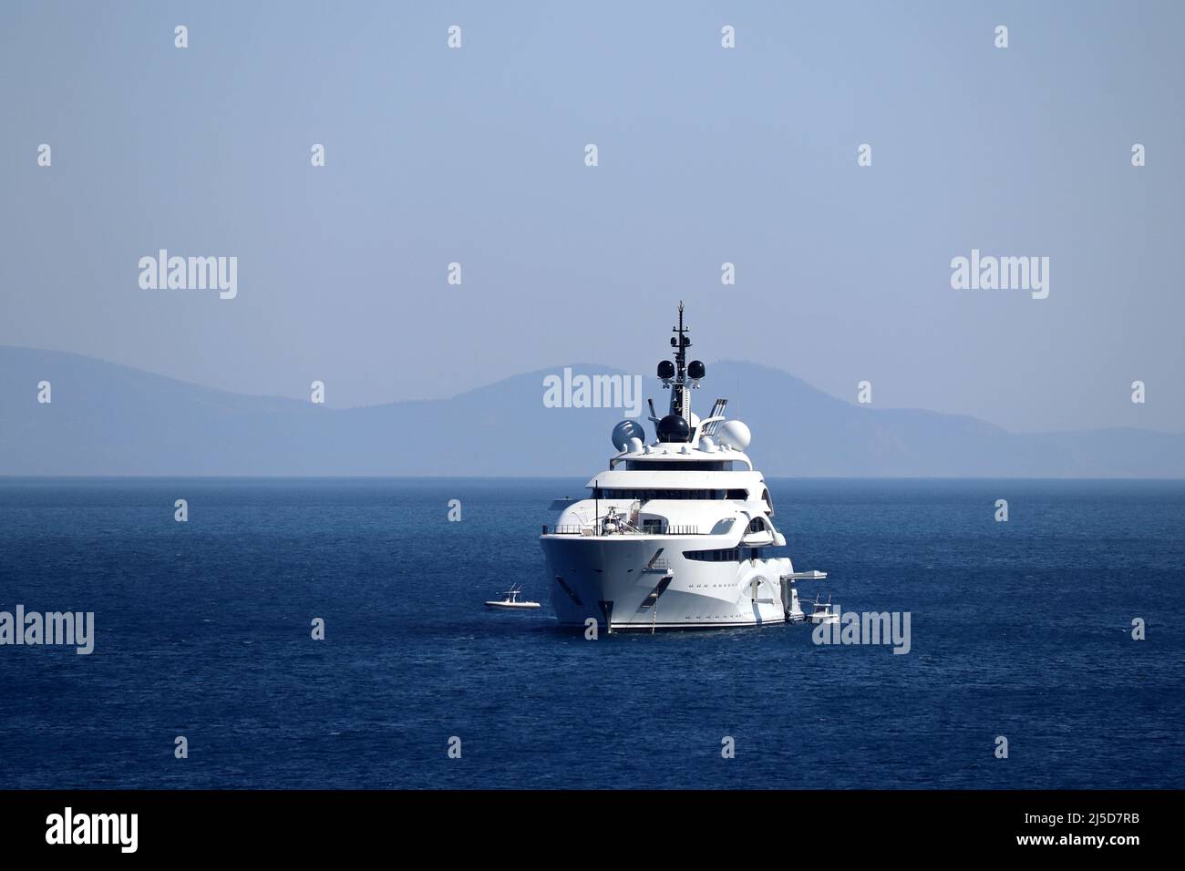 Yacht de luxe avec héliport et hélicoptère naviguant dans une mer, vue de face. Bateau blanc sur fond d'île de montagne Banque D'Images