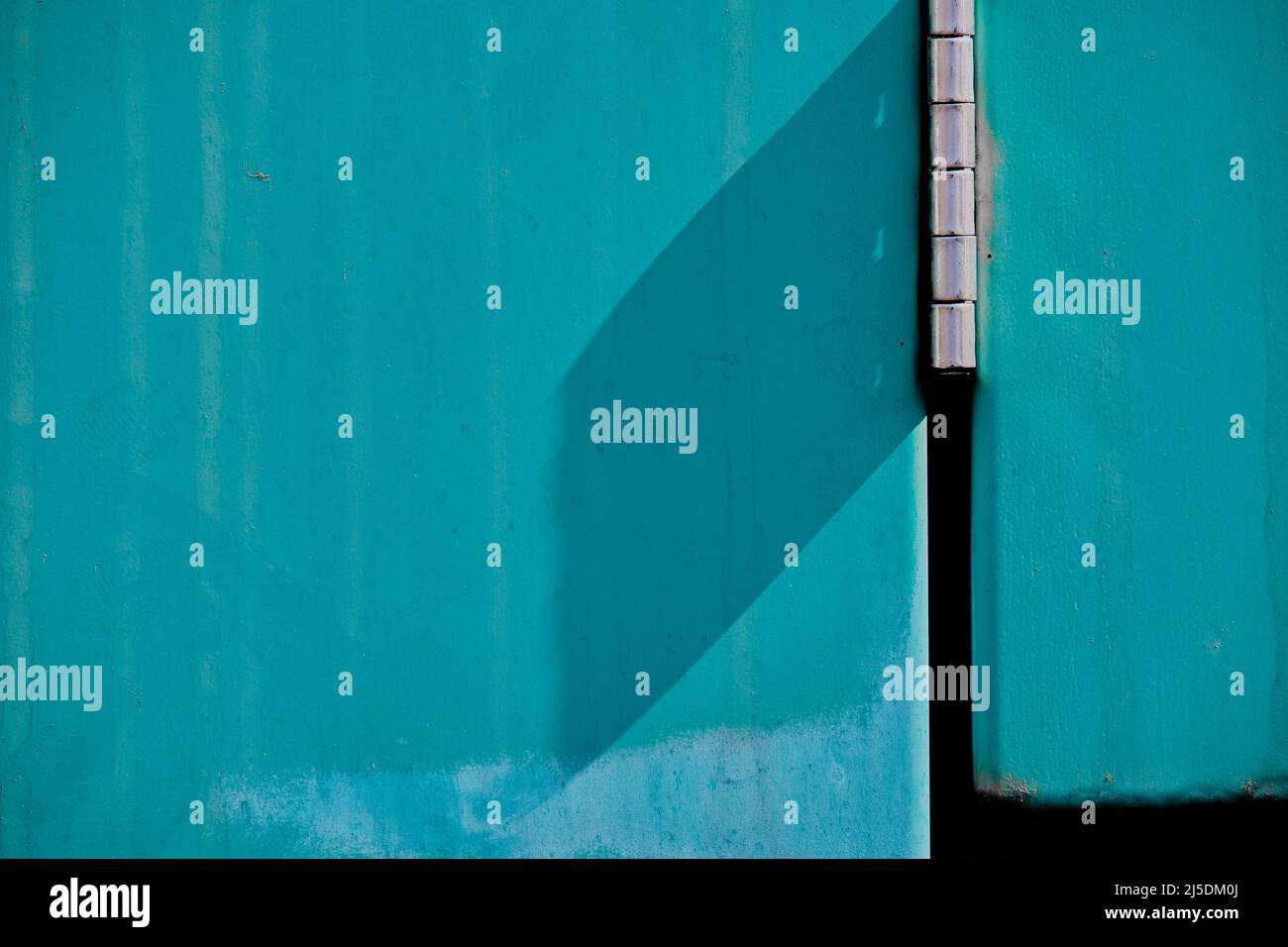 Résumé : porte en métal turquoise avec charnière chromée vue en gros plan. Porte extérieure striée avec des lignes verticales très probablement créées par la pluie. Banque D'Images