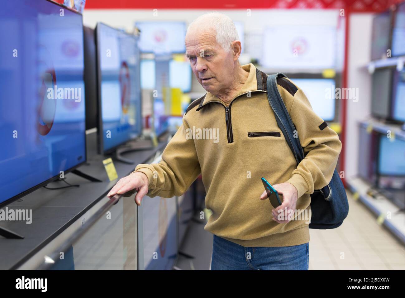 Homme âgé qui choisit un téléviseur dans la salle d'exposition du magasin d'électronique Banque D'Images