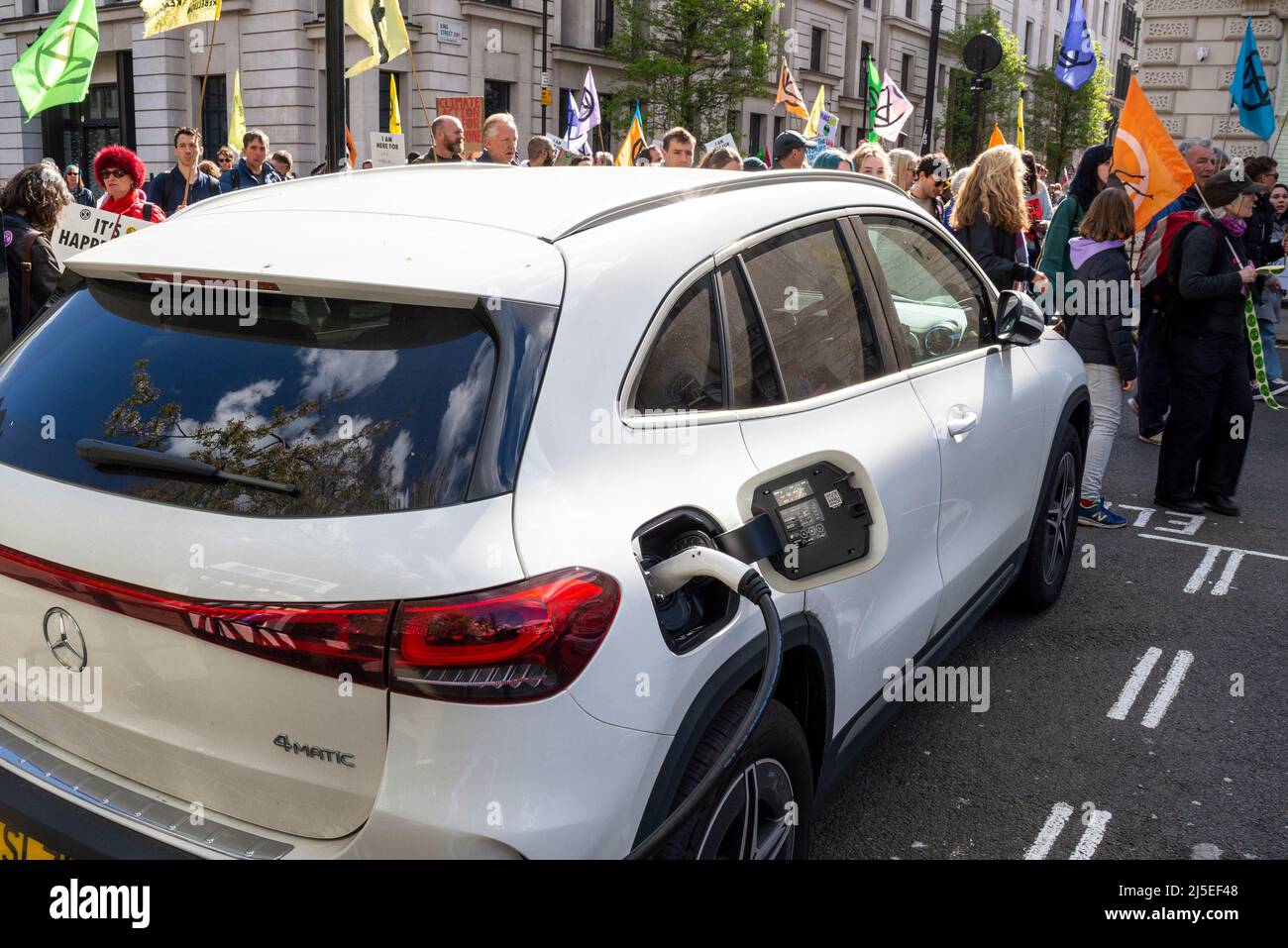 Extinction les manifestants de la rébellion passent devant une voiture électrique en charge à un point de recharge, se dirigeant vers le siège de BP pour protester contre les combustibles fossiles Banque D'Images