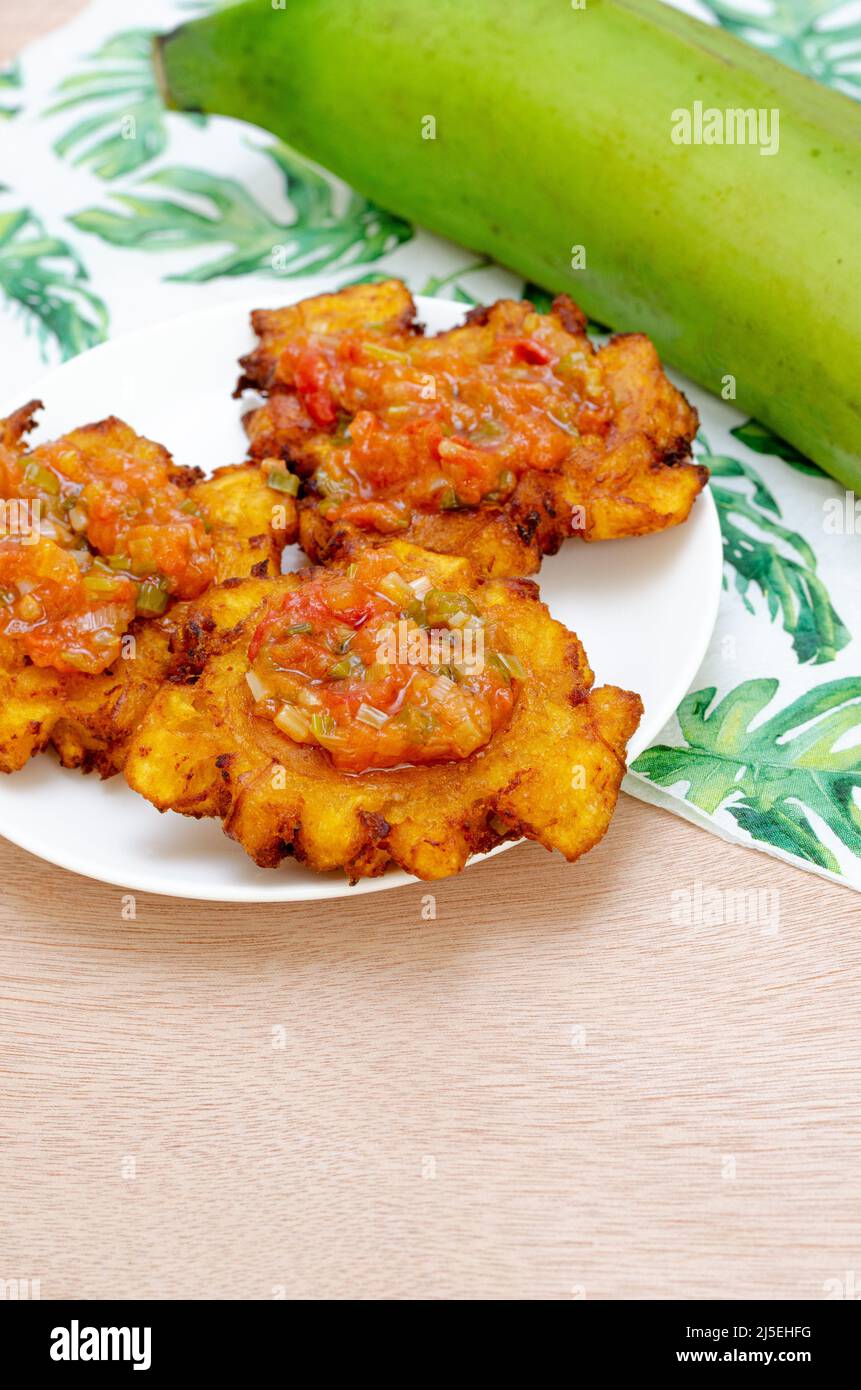 Patacones ou tostones frits de plantain vert ou mûr, croustillants, avec ragoût de tomate et d'oignon appelé « hogado ». Cuisine colombienne traditionnelle, sur un bois clair. Banque D'Images