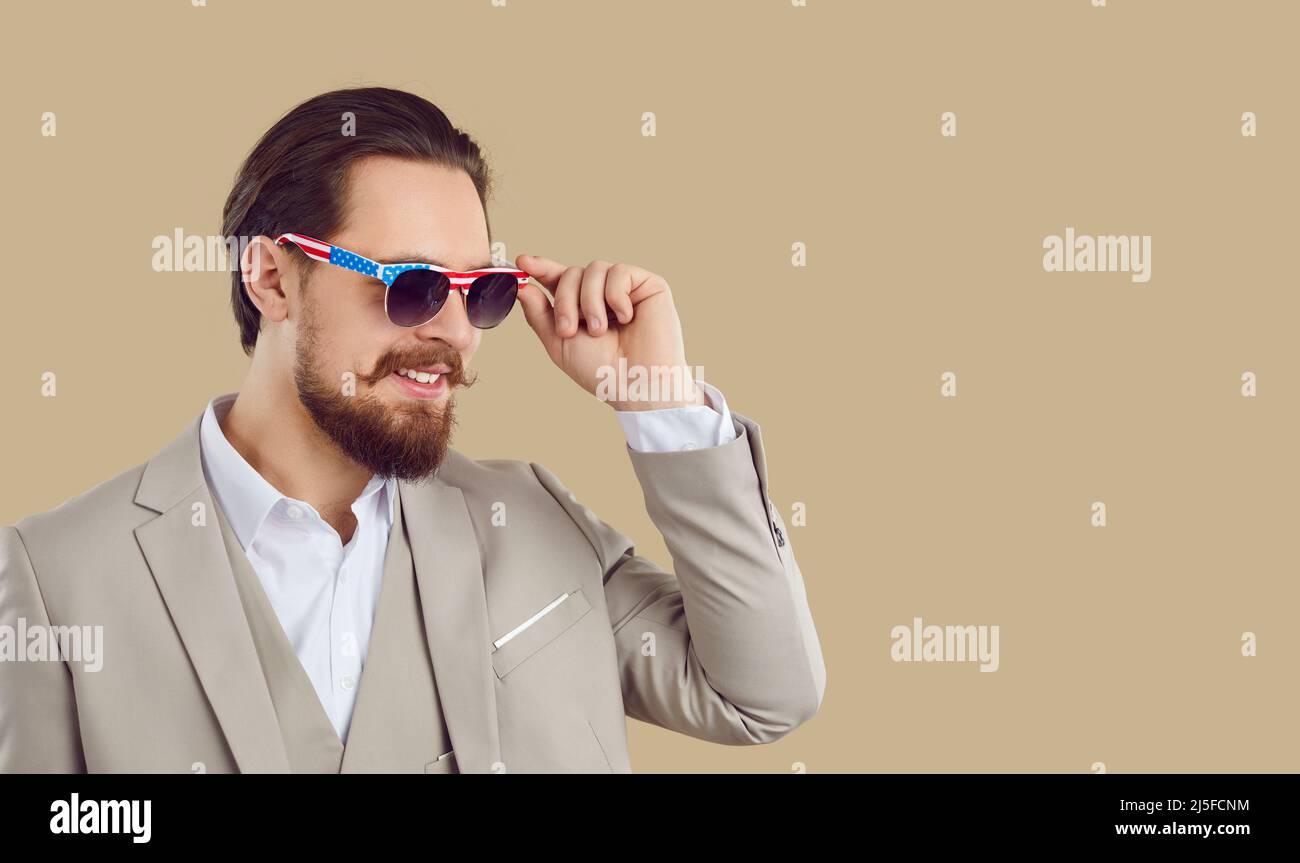 Beau homme en costume et lunettes de soleil avec motif drapeau américain sur fond beige espace copie Banque D'Images