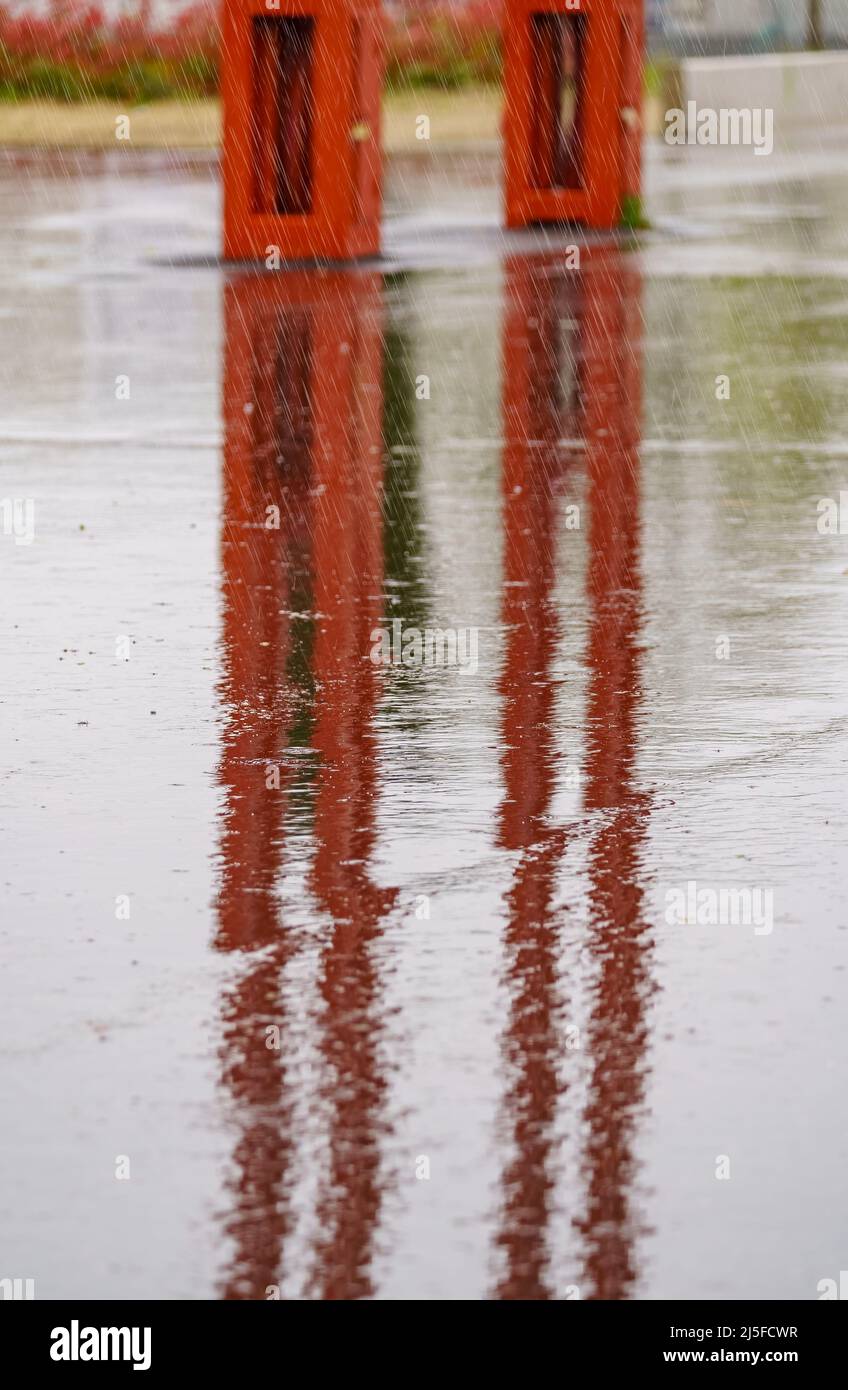 Forte pluie tombant sur le sol et formant des réflexions avec des meubles de rue. Banque D'Images