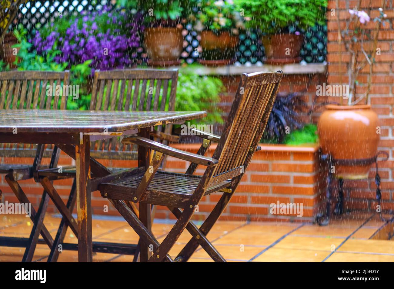 Forte pluie tombant sur le mobilier de jardin en bois de teck et plantes à fleurs. Banque D'Images