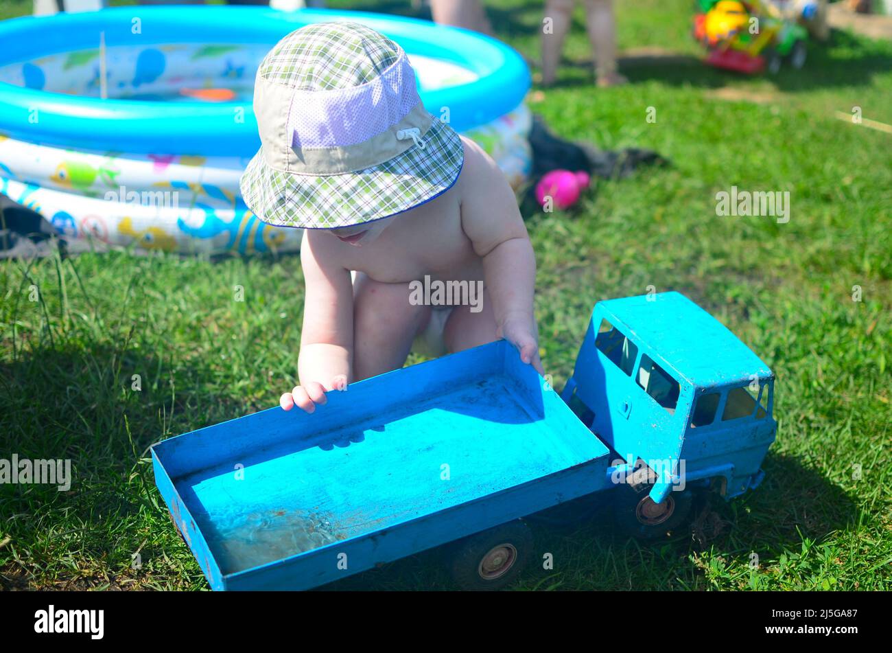 concept de jeux d'été pour enfants - un garçon dans un chapeau panama aucun visage joue avec un camion bleu jouet sur l'herbe verte. Banque D'Images