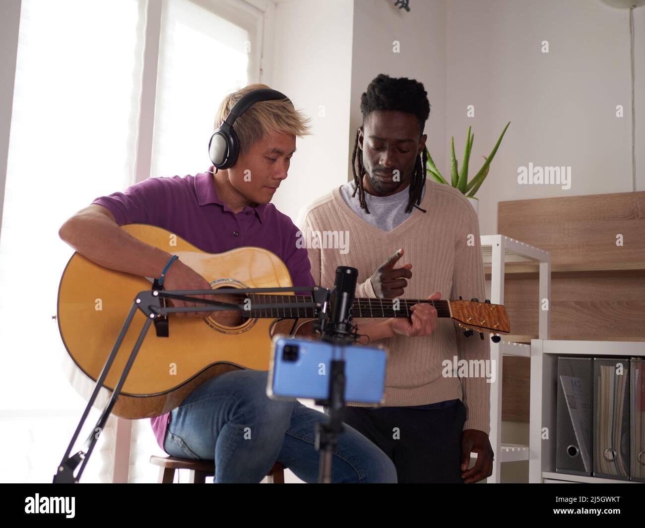 Un tuteur afroamerican personnel explique à son étudiant asiatique comment jouer la corde étudiée correctement. Éducation musicale à la maison Banque D'Images