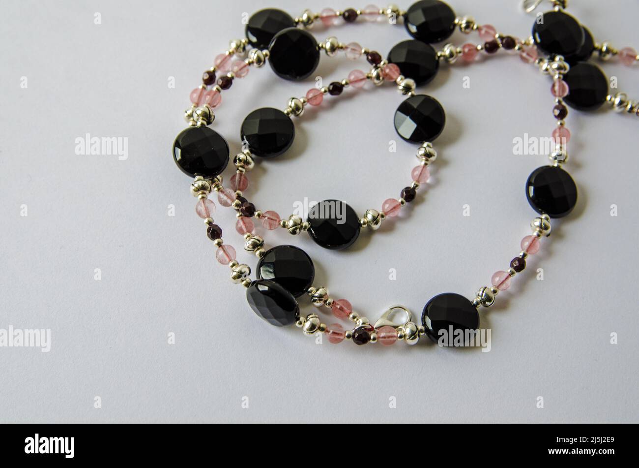 Un collier fait à la main à partir de perles d'obsidienne, de grenat et de quartz fraise enroulé sur un fond blanc avec ombre portée. Banque D'Images