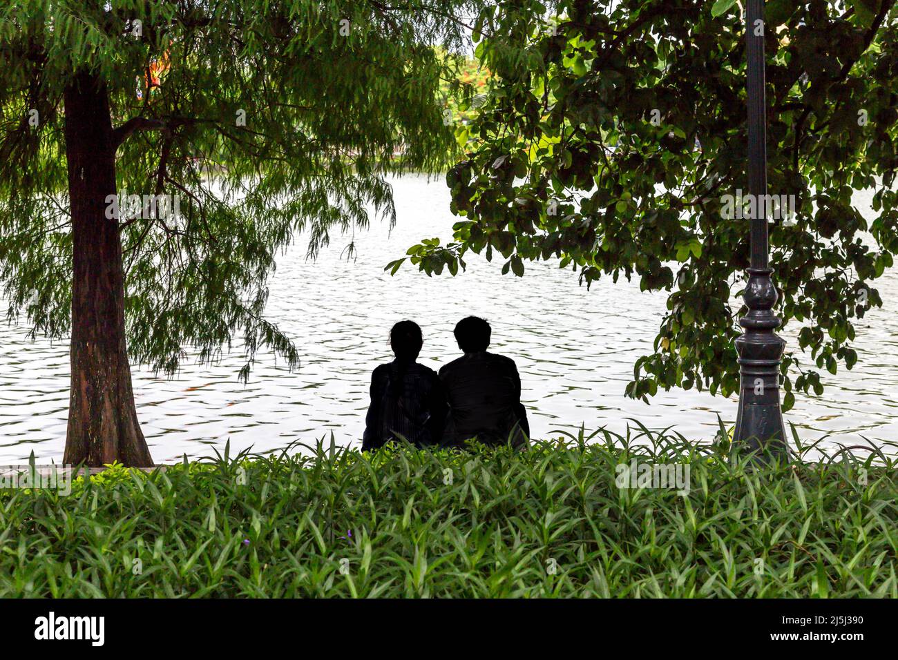 Deux personnes ensemble assis dans l'herbe regardant le lac dans le vieux quartier, Hanoi. Banque D'Images