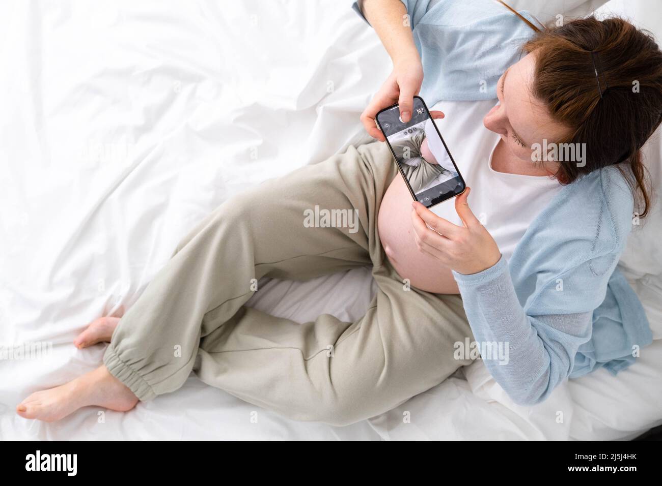 Femme enceinte expectative faisant la photo de son grand ventre au téléphone. Femme photographiant l'enfant en attente, assis sur le lit. Le grand ventre a avancé la grossesse Banque D'Images