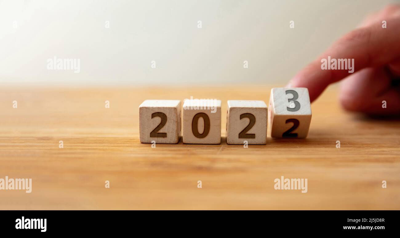De 2022 à 2023 Bonne Année. Le doigt retourne le dernier chiffre sur le cube en bois changeant l'année sur la table en bois. Nouveau plan, affaires, carrière, cible, su Banque D'Images